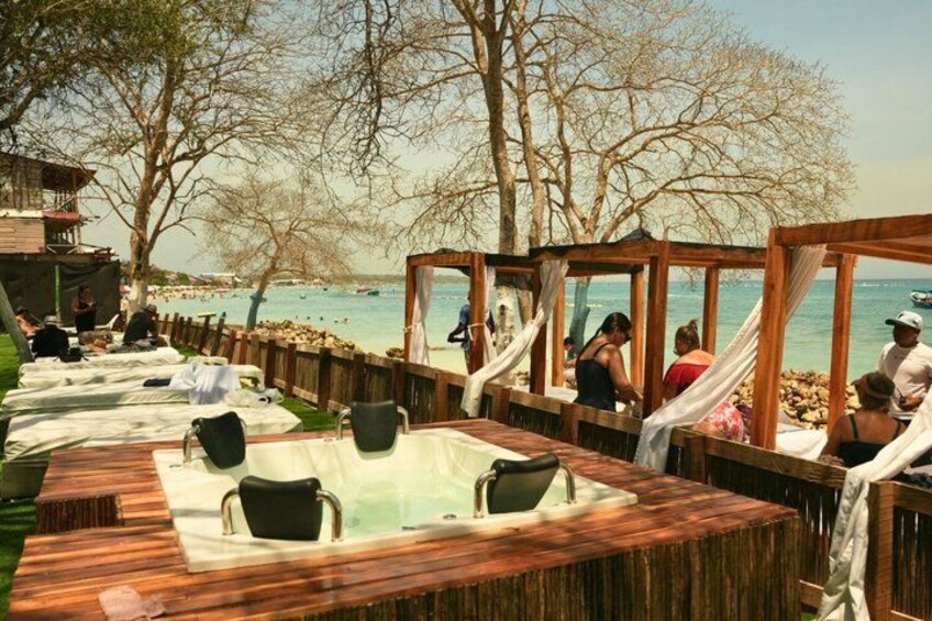 A wooden deck with hot tubs and chairs, overlooking a body of water. 2