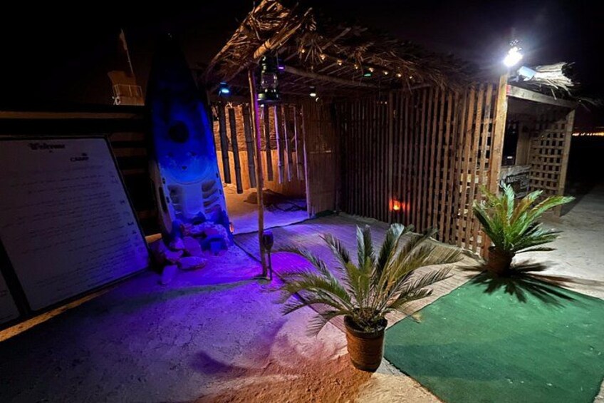 A tiki hut with a thatched roof, a surfboard, and a potted plant. 2