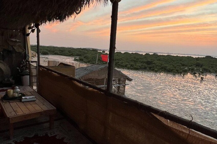 A wooden deck overlooking a body of water with a thatched roof structure and a small building in the background. 4