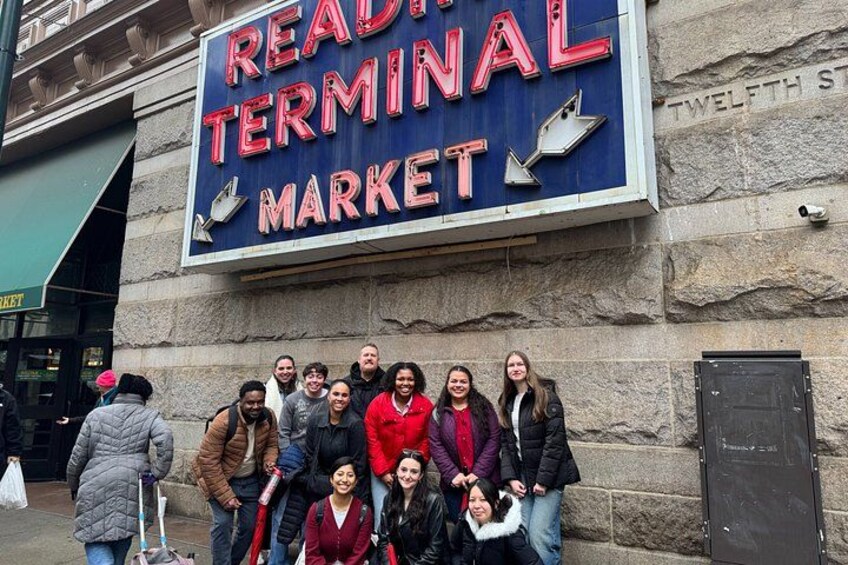 A group of people posing in front of a sign that reads 'READING TERMINAL MARKET.' 1