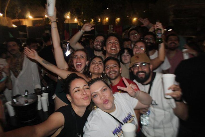 A group of people at a social gathering, possibly a party or celebration, with some holding drinks and others making gestures. 2