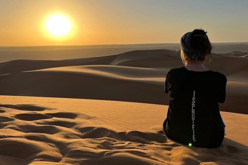Eine Person sitzt auf Dünen, während die Sonne im Hintergrund untergeht. 4