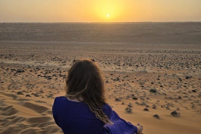 Eine Person sitzt auf einer Sanddüne, im Hintergrund ein Sonnenuntergang. 3