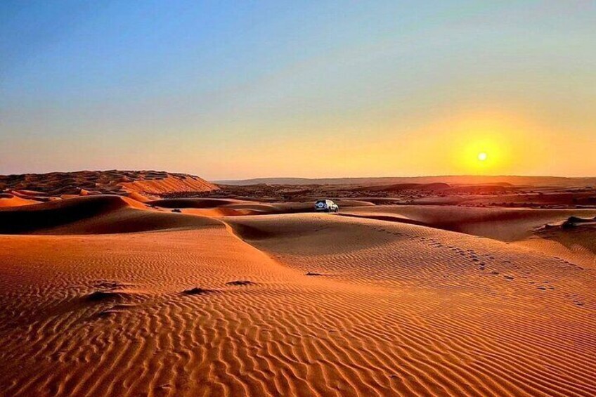 Wüstenlandschaft mit Sanddünen und einem Fahrzeug bei Sonnenuntergang. 1