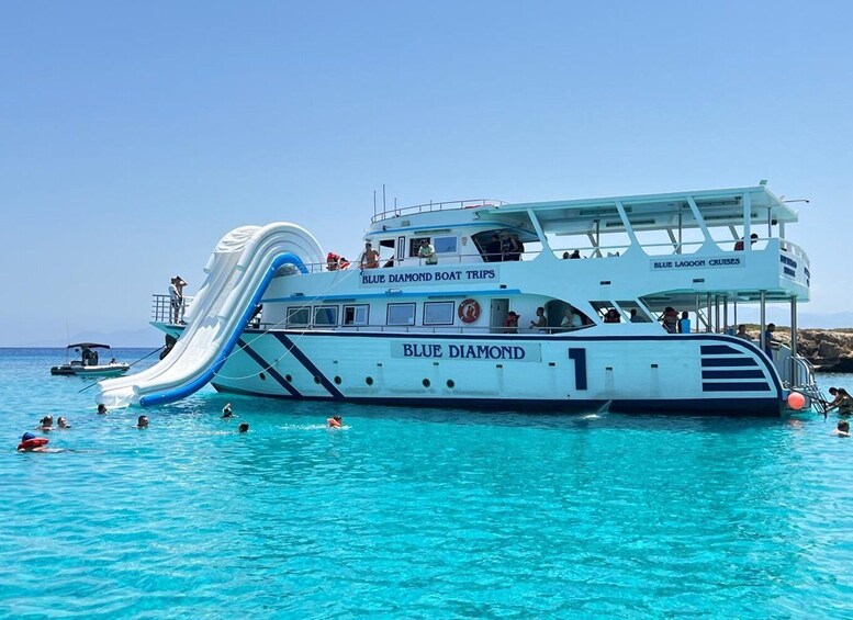 Un bateau blanc baptisé « Blue Diamond », doté d’un toboggan bleu et blanc, est entouré de personnes qui nagent dans une eau d’un bleu cristallin. 3