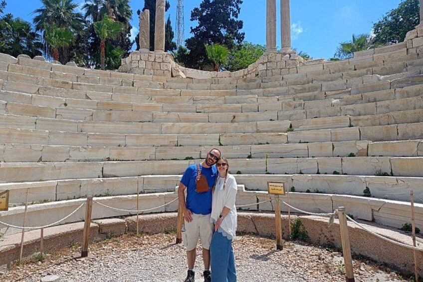 A stone amphitheater with tiered seating, a person in a blue shirt, and another in a white shirt. 3