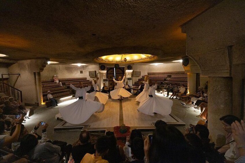 A dance performance in a dimly lit room with a circular stage and an audience seated around it. 3