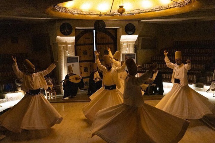 A group of people in traditional attire performing a dance in a room with bookshelves and a large window. 1