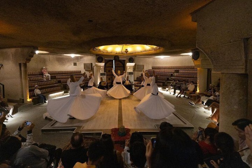 A dance performance in a dimly lit room with an audience seated around the performers. 2