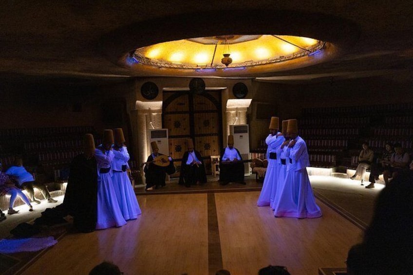 A group of people in white robes performing in a dimly lit room with a wooden floor and a large circular stained glass window. 4