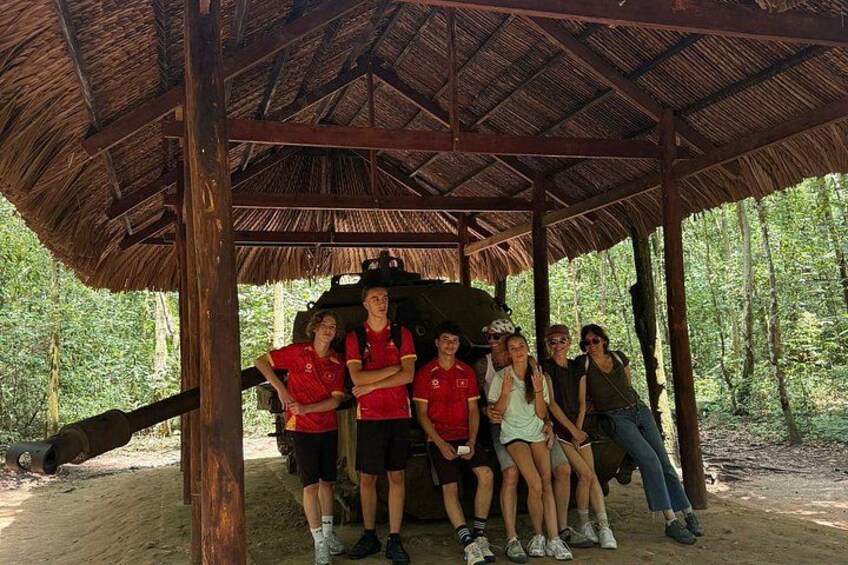Un grupo de personas posando bajo una estructura con techo de paja en un área boscosa. 1