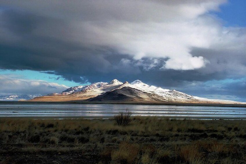 A snow-capped mountain range with a flat-topped peak, a body of water in the foreground, and a cloudy sky. 2