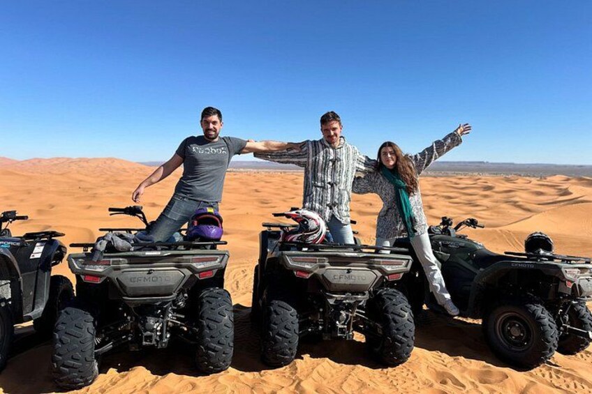 Three people on ATVs in a desert with sand dunes in the background. 4