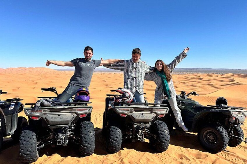 Three people on ATVs in a desert with sand dunes in the background. 2