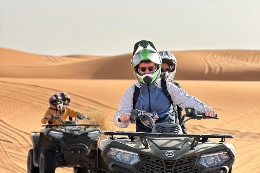 Two people riding ATVs on a sandy dune landscape. 1