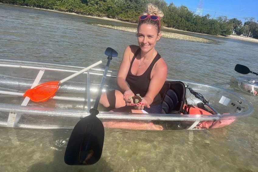 A person in a transparent kayak on a body of water with paddle and oar visible. 3