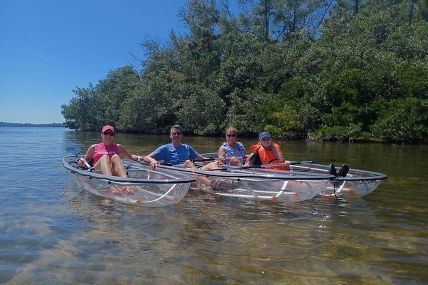 Three people in a transparent boat on a calm body of water surrounded by trees. 5