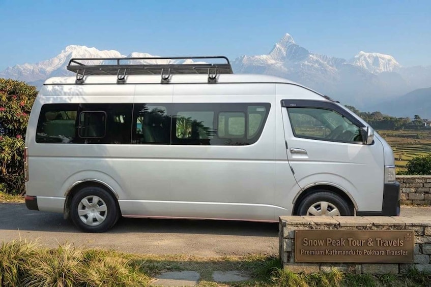 Un fourgon blanc était garé devant un panneau indiquant : « Snow Peak Tour & Travels, service de transfert de qualité supérieure de Katmandou à Pokhara. » 2