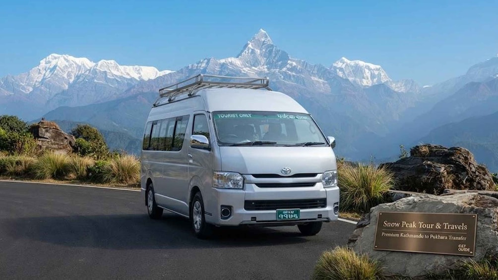 Un fourgon blanc équipé d’un porte-bagages sur le toit est garé sur une route, avec un paysage montagneux en arrière-plan. 4