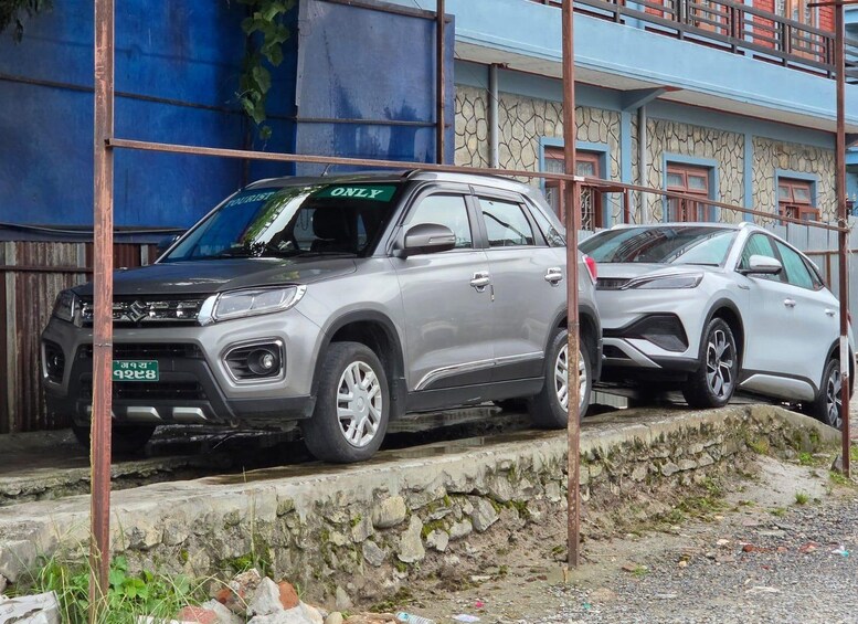 A silver SUV parked on a stone-paved area with a blue wall and a building in the background. 2