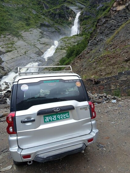 A white SUV parked on a rocky path with a waterfall in the background. 4
