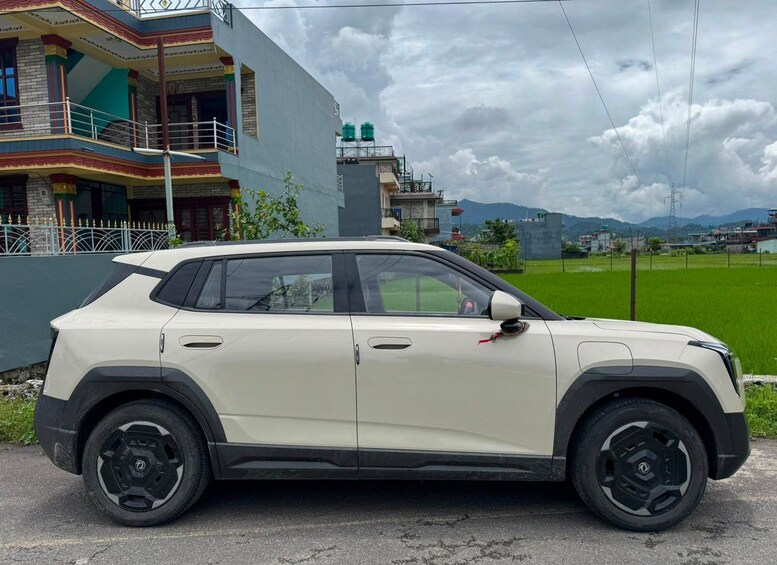 A white SUV parked in front of a building with a green field and mountains in the background. 3