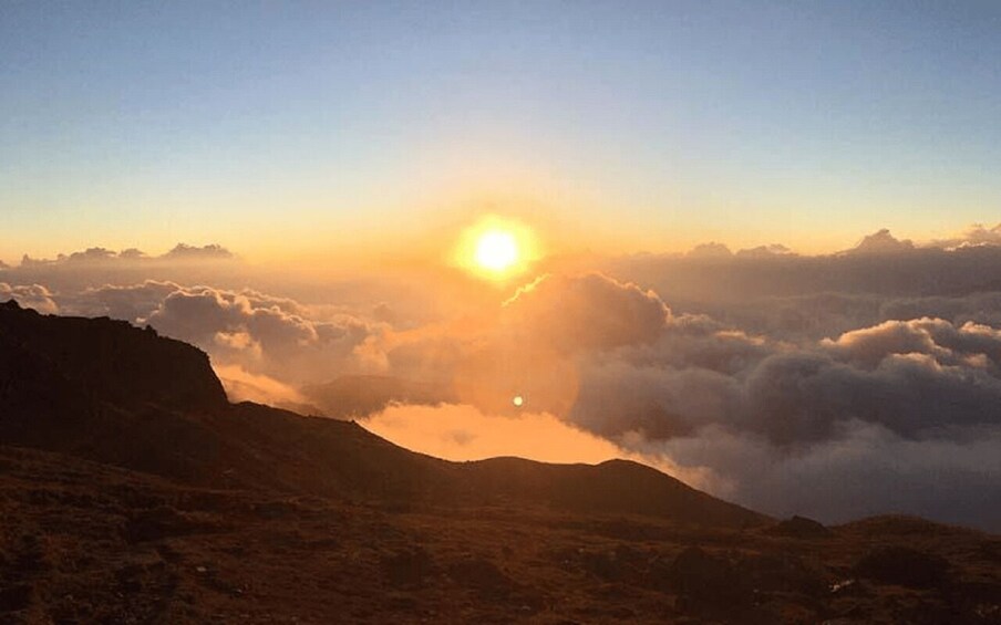 A sunrise over a mountainous landscape with clouds below. 3