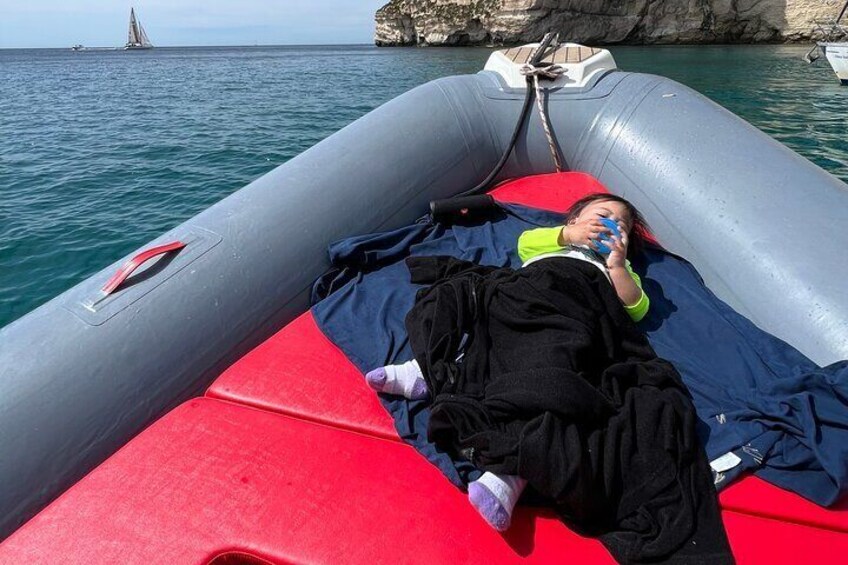 A person lying on an inflatable boat with a rocky coastline in the background. 4