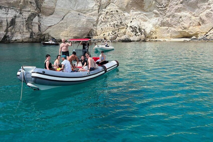 A group of people on a small boat in clear blue water near rocky cliffs. 4