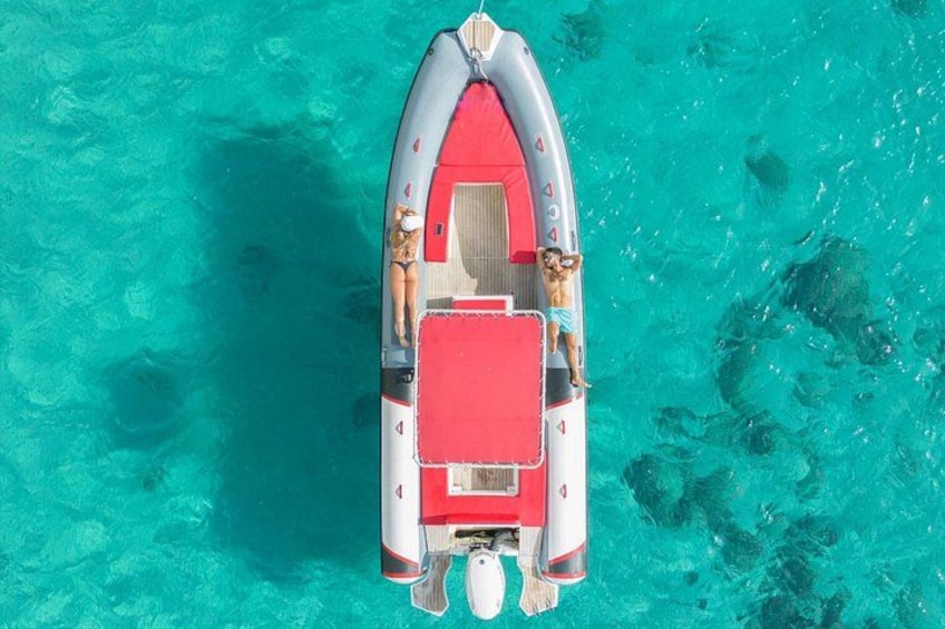 A small inflatable boat with a red deck, two people, and a dog on a turquoise sea. 1