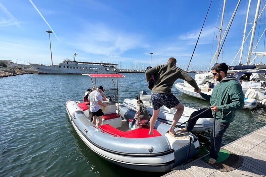 A group of people on a small inflatable boat at a marina with other boats and a large ship in the background. 5
