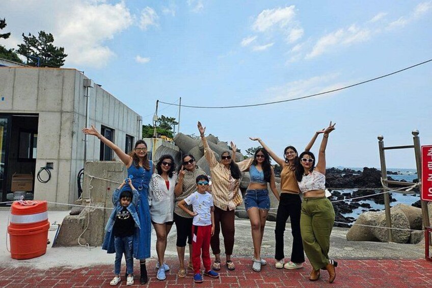 Un grupo de personas posando al aire libre con una costa rocosa y un edificio en el fondo. 4