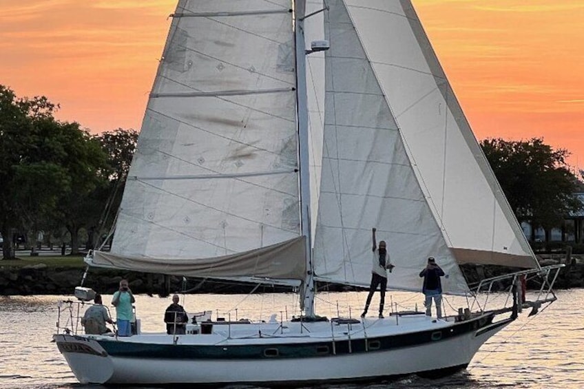 A sailboat with a large sail on calm water during sunset. 3
