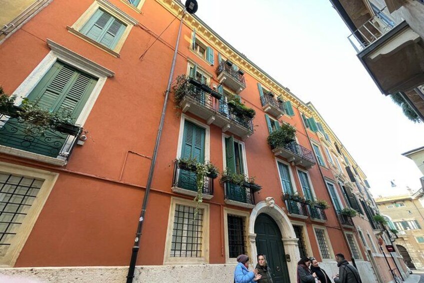 Un edificio rojo con contraventanas verdes y balcones con plantas. 5