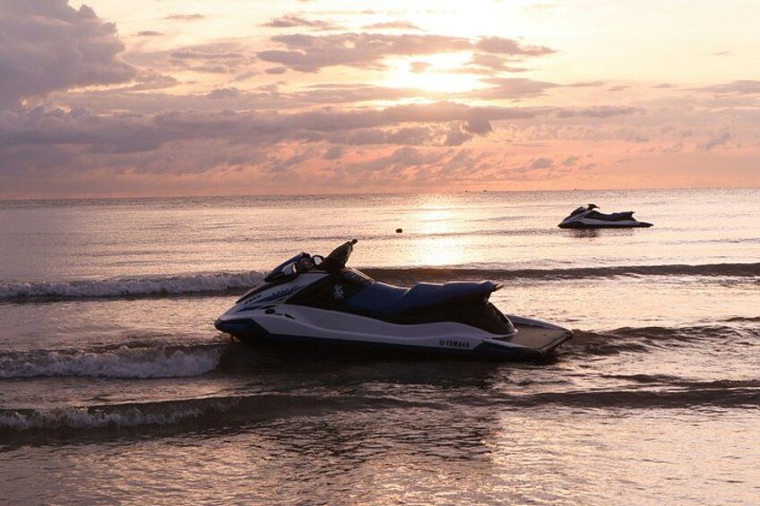 Un jet ski en la playa al atardecer, con olas y otro jet ski a lo lejos. 3