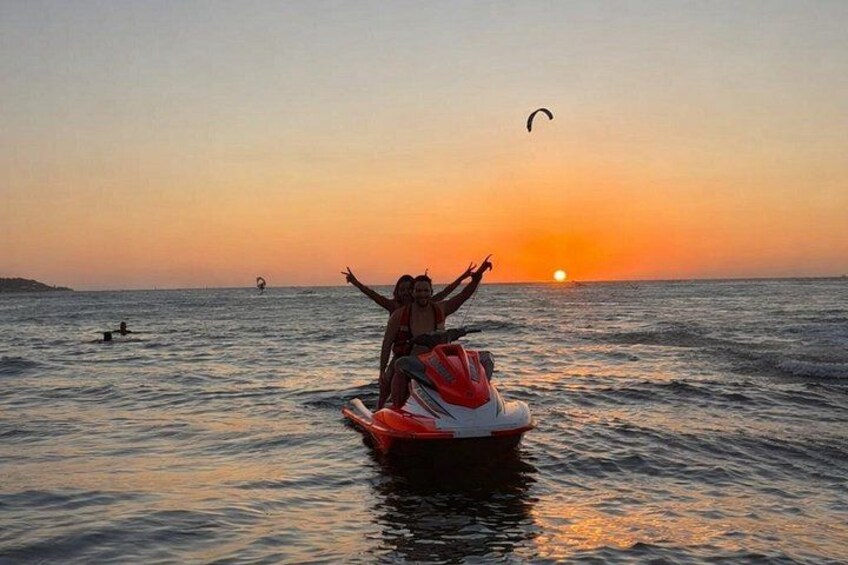 Un atardecer sobre el océano, con una persona en un jet ski y otra persona parapenteando al fondo. 4