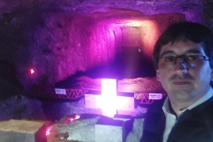 A person standing in front of a cave with a cross and some red lights. 1