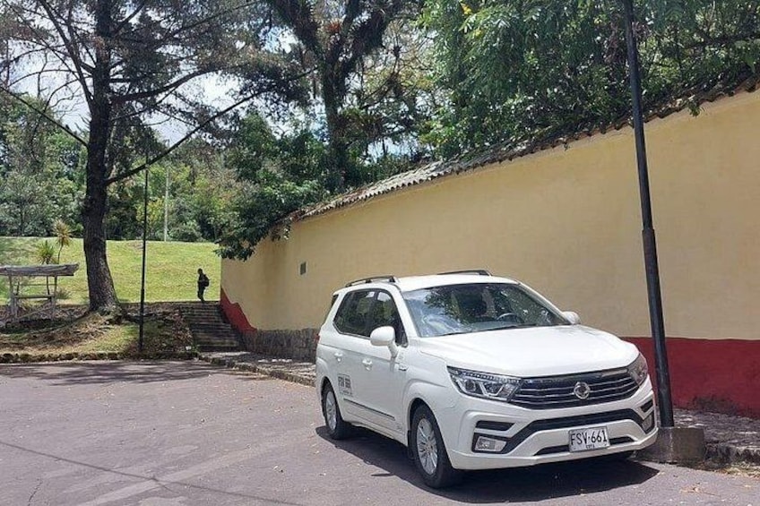 A white SUV parked on a paved area with a beige wall and a tree in the background. 5