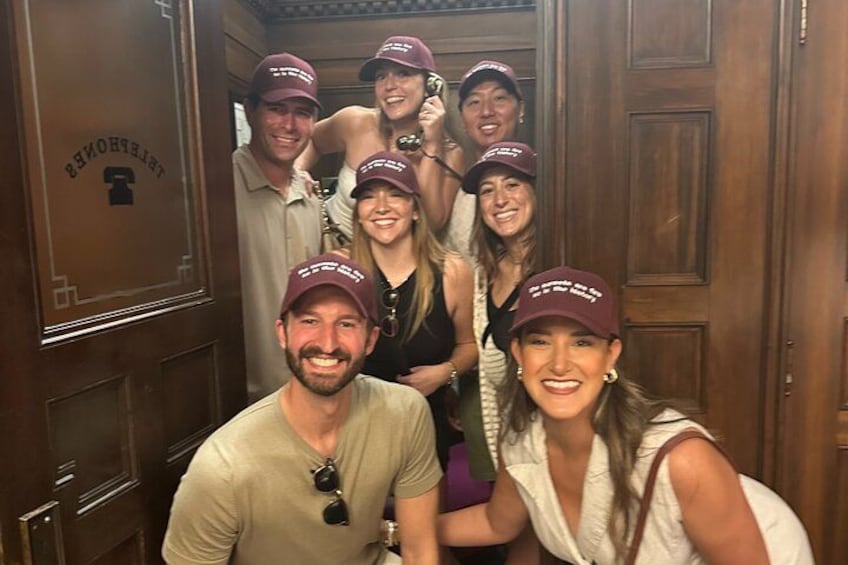A group of people inside a wooden elevator with a sign that reads 'LIBERTY HALL.' 3