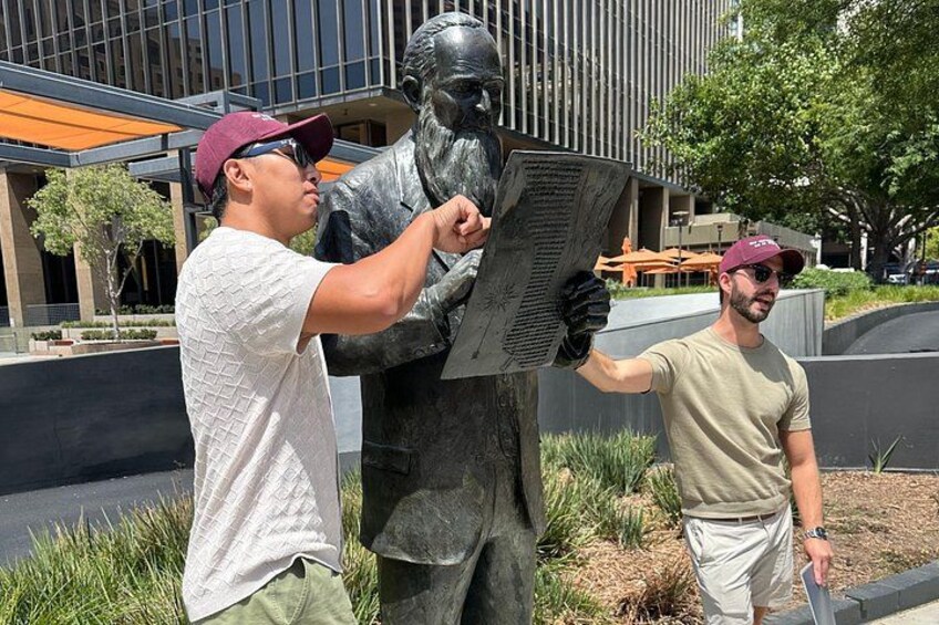 Two people interacting with a statue outdoors, with modern architecture in the background. 2