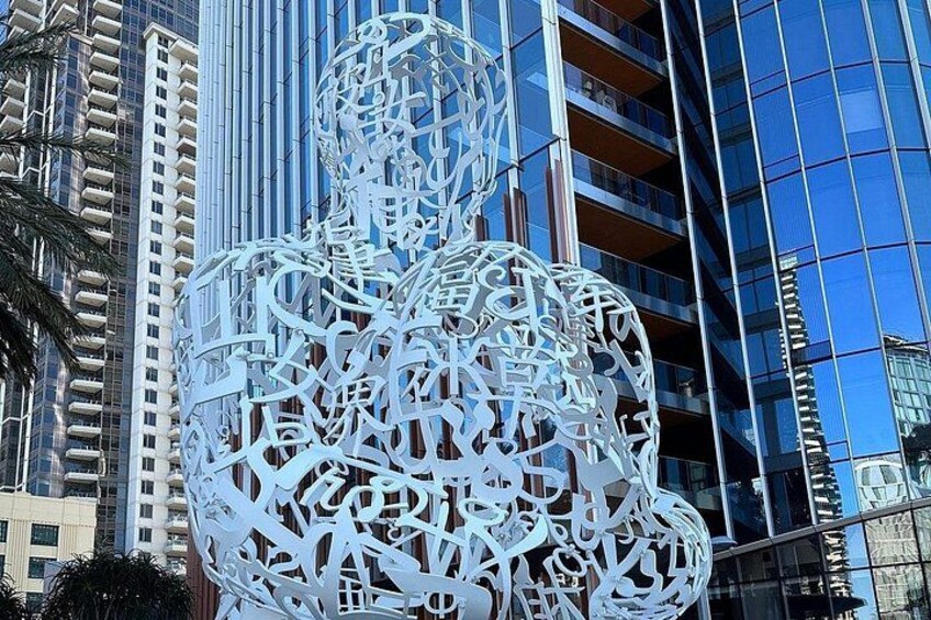 A large white abstract sculpture in an urban setting with modern buildings in the background. 3