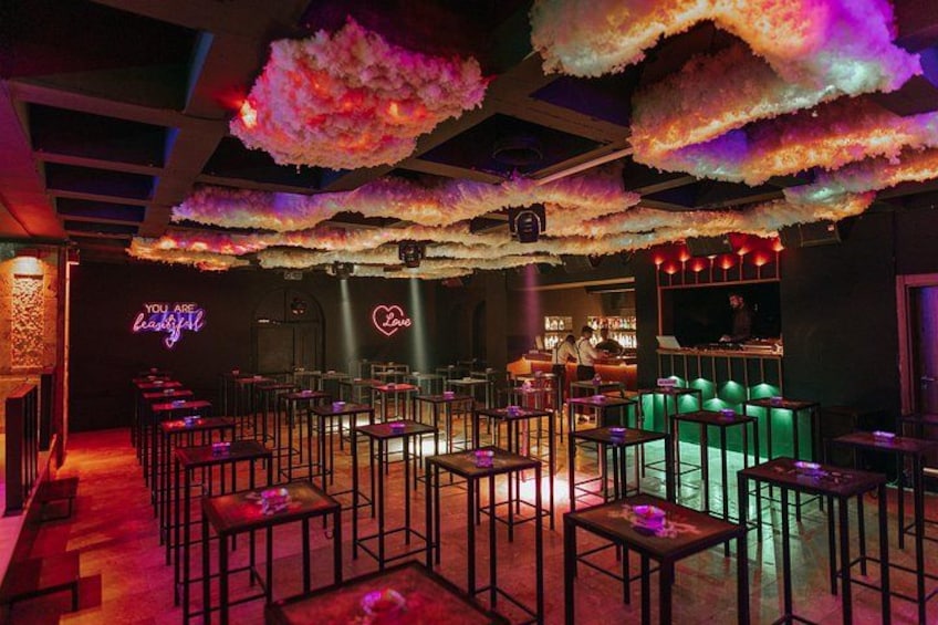 A bar with cloud-like ceiling decorations, a neon sign, and a bar counter. 2