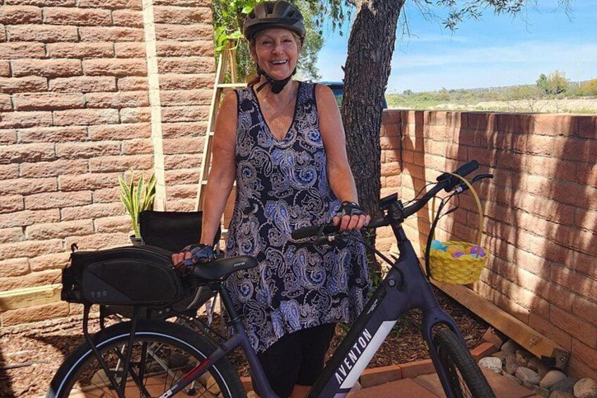A person standing next to a bicycle with a basket and a bag, in an outdoor setting with a brick wall and a wooden fence. 4