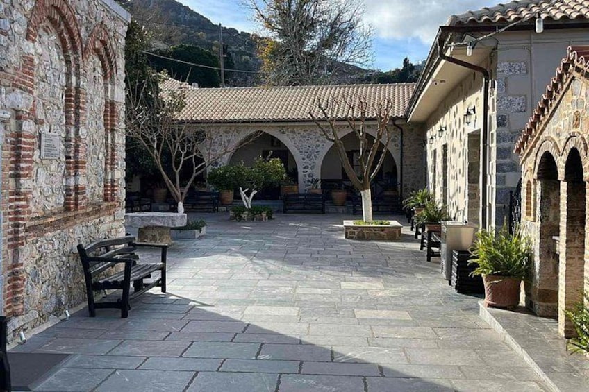 A courtyard with stone flooring, a bench, potted plants, and a building with arches. 4