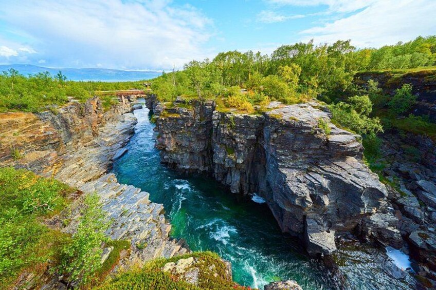 A river flowing through a rocky gorge with a bridge in the distance. 1