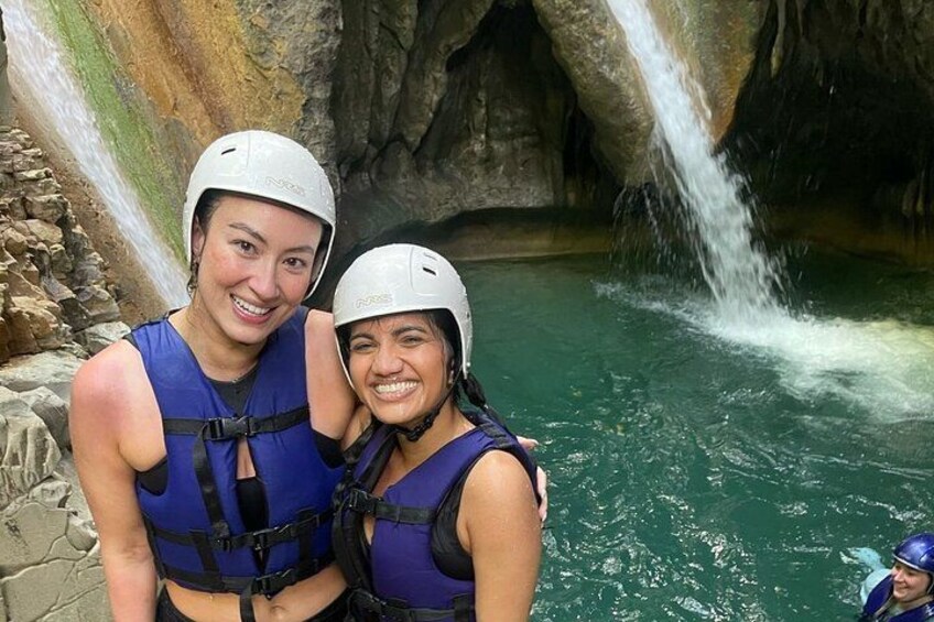 Two people wearing helmets and life vests near a waterfall in a cave. 3