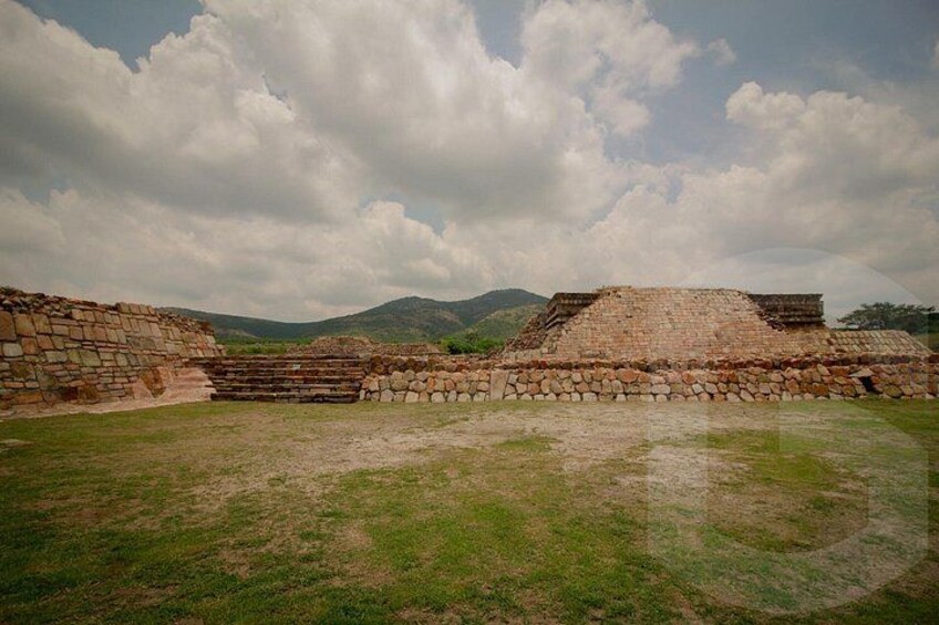 Ancient stone ruins with stepped pyramids and a grassy field. 1