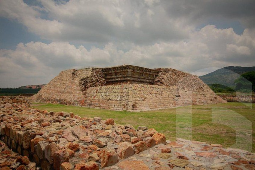 A large ancient pyramid with a stepped structure, surrounded by a grassy area and a stone wall. 1