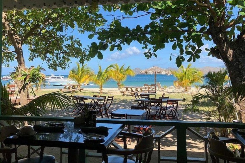 An outdoor dining area with tables and chairs, overlooking a beach with palm trees and a view of the ocean. 4