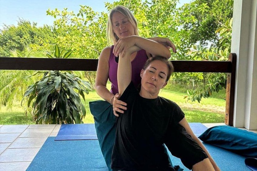 A person receiving a massage on a blue mat outdoors with a wooden deck and greenery in the background. 1